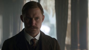 Movie still from “The Alienist” (2018), created by Cary Joji Fukunaga – A person wearing a suit and tie; Close Up shot, Low angle