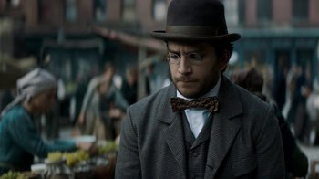 Movie still from “The Alienist” (2018), created by Cary Joji Fukunaga – A man wearing a suit and a bow tie; Close Up shot, Over the shoulder angle