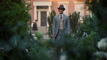Movie still from “The Alienist” (2018), created by Cary Joji Fukunaga – A man in a suit and hat standing in a flower garden; Wide shot, Over the shoulder angle