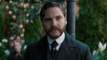Movie still from “The Alienist” (2018), created by Cary Joji Fukunaga – A man in a suit and tie standing next to a pole; Close Up shot, Low angle