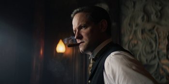 Movie still from “The Alienist” (2018), created by Cary Joji Fukunaga – A man in a vest and tie smoking a cigar; Close Up shot, Low angle