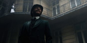 Movie still from “The Alienist” (2018), created by Cary Joji Fukunaga – A man in a suit and hat standing in front of a building; Medium shot, Low angle
