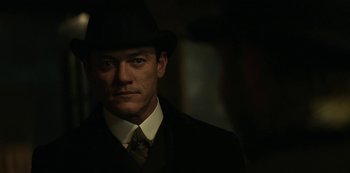 Movie still from “The Alienist” (2018), created by Cary Joji Fukunaga – A man wearing a suit and a hat in the dark; Close Up shot, Over the shoulder angle