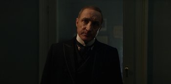 Movie still from “The Alienist” (2018), created by Cary Joji Fukunaga – An older man in a suit and tie in front of a door; Close Up shot, Low angle