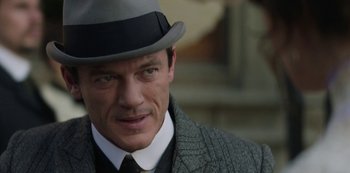 Movie still from “The Alienist” (2018), created by Cary Joji Fukunaga – A person wearing a hat and a suit; Close Up shot, Over the shoulder angle
