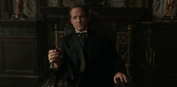 Movie still from “The Alienist” (2018), created by Cary Joji Fukunaga – A man wearing a suit and tie in a dark room; Medium shot, Low angle