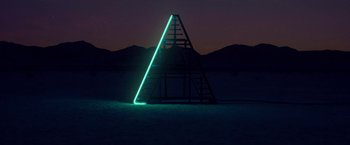 Movie still from “The Bad Batch” (2016), directed by Ana Lily Amirpour – An illuminated triangle structure in the middle of the night; Extreme Wide shot, Overhead angle