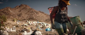 Movie still from “The Bad Batch” (2016), directed by Ana Lily Amirpour – A person walking through a trash pile with a basket; Medium shot, Low angle