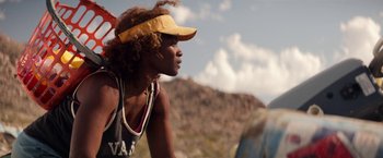 Movie still from “The Bad Batch” (2016), directed by Ana Lily Amirpour – A woman in a yellow hat is looking off into the distance; Close Up shot, Over the shoulder angle