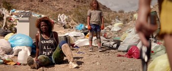 Movie still from “The Bad Batch” (2016), directed by Ana Lily Amirpour – A young girl standing next to an older woman; Medium shot, Low angle