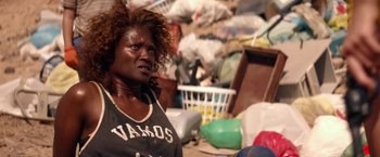 Movie still from “The Bad Batch” (2016), directed by Ana Lily Amirpour – A woman standing next to a pile of trash; Close Up shot, Over the shoulder angle