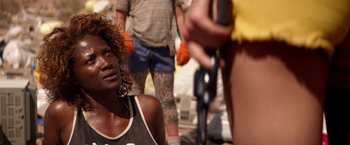 Movie still from “The Bad Batch” (2016), directed by Ana Lily Amirpour – A woman sitting on the ground in front of other people; Close Up shot, Over the shoulder angle