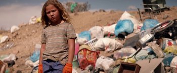 Movie still from “The Bad Batch” (2016), directed by Ana Lily Amirpour – A young girl standing in front of a pile of garbage; Medium shot, Low angle
