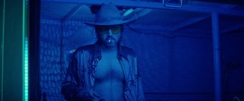 Movie still from “The Bad Batch” (2016), directed by Ana Lily Amirpour – A man with a hat and sunglasses in the dark; Medium shot, Low angle