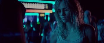 Movie still from “The Bad Batch” (2016), directed by Ana Lily Amirpour – A woman in white shirt standing next to neon lights; Close Up shot, Over the shoulder angle