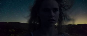 Movie still from “The Bad Batch” (2016), directed by Ana Lily Amirpour – A woman with long dark hair is looking at the camera; Close Up shot, Low angle