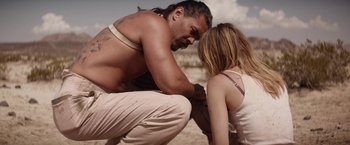Movie still from “The Bad Batch” (2016), directed by Ana Lily Amirpour – A man kneeling down next to a woman on the beach; Medium shot, Over the shoulder angle