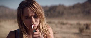 Movie still from “The Bad Batch” (2016), directed by Ana Lily Amirpour – A woman is smoking a cigarette in the desert; Close Up shot, High angle
