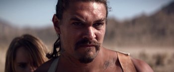 Movie still from “The Bad Batch” (2016), directed by Ana Lily Amirpour – A person with long hair and a beard; Close Up shot, Low angle