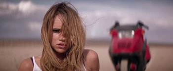 Movie still from “The Bad Batch” (2016), directed by Ana Lily Amirpour – A woman with long blonde hair standing next to a motorcycle; Close Up shot, Low angle