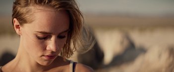 Movie still from “The Bad Batch” (2016), directed by Ana Lily Amirpour – A woman's face with a herd of cattle in the background; Close Up shot, Over the shoulder angle
