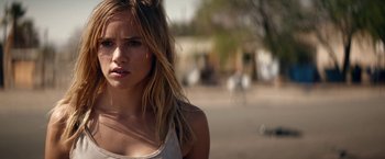 Movie still from “The Bad Batch” (2016), directed by Ana Lily Amirpour – A beautiful young woman standing next to a street; Close Up shot, Over the shoulder angle