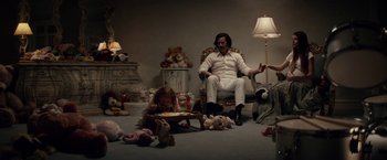 Movie still from “The Bad Batch” (2016), directed by Ana Lily Amirpour – A man sitting in a chair next to a child; Wide shot, High angle