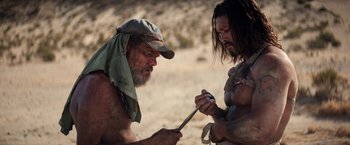 Movie still from “The Bad Batch” (2016), directed by Ana Lily Amirpour – Two men in the desert looking at a cell phone; Medium shot, Low angle