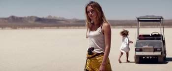 Movie still from “The Bad Batch” (2016), directed by Ana Lily Amirpour – A beautiful young woman standing on top of a sandy beach; Medium shot, Over the shoulder angle