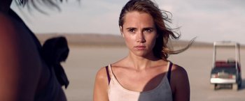 Movie still from “The Bad Batch” (2016), directed by Ana Lily Amirpour – A beautiful young woman standing on top of a sandy beach; Close Up shot, Over the shoulder angle