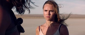 Movie still from “The Bad Batch” (2016), directed by Ana Lily Amirpour – A woman standing in the sand looking angry; Close Up shot, Over the shoulder angle