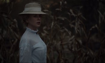 Movie still from “The Beguiled” (2017), directed by Sofia Coppola – A woman wearing a hat standing in front of a bush; Medium shot, Over the shoulder angle