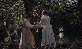 Movie still from “The Beguiled” (2017), directed by Sofia Coppola – Two women holding hands in front of a tree; Medium shot, Over the shoulder angle