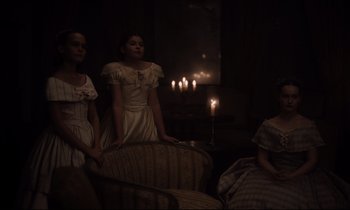 Movie still from “The Beguiled” (2017), directed by Sofia Coppola – A group of people sitting in a living room with lit candles; Medium shot, High angle