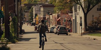 Movie still from “The Book of Henry” (2017), directed by Colin Trevorrow – A person riding a bike down a street; Wide shot, Over the shoulder angle