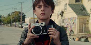 Movie still from “The Book of Henry” (2017), directed by Colin Trevorrow – A young boy holding a camera while standing on the side of the road; Close Up shot, Low angle