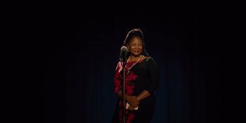 Movie still from “The Book of Henry” (2017), directed by Colin Trevorrow – A woman standing in front of a microphone on a stage; Medium shot, Low angle
