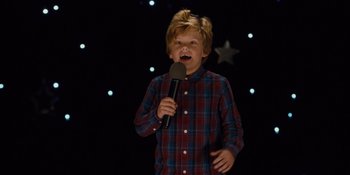 Movie still from “The Book of Henry” (2017), directed by Colin Trevorrow – A young boy holding a microphone in front of a star background; Medium shot, High angle