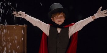 Movie still from “The Book of Henry” (2017), directed by Colin Trevorrow – A young boy wearing a top hat and holding his arms up; Medium shot, Low angle
