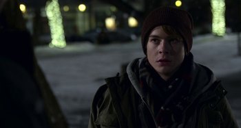 Movie still from “The Christmas Chronicles” (2018), directed by Clay Kaytis – A young man in winter clothing standing on a sidewalk; Close Up shot, Over the shoulder angle