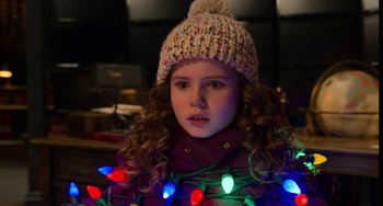 Movie still from “The Christmas Chronicles” (2018), directed by Clay Kaytis – A little girl wearing a hat and a sweater with christmas lights around her neck; Close Up shot, Over the shoulder angle
