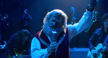 Movie still from “The Christmas Chronicles” (2018), directed by Clay Kaytis – An old man with a long beard is holding a microphone; Medium shot, Low angle