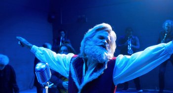 Movie still from “The Christmas Chronicles” (2018), directed by Clay Kaytis – An old man with a long white beard singing into a microphone in front of a group of people; Medium shot, Low angle