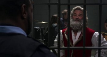 Movie still from “The Christmas Chronicles” (2018), directed by Clay Kaytis – A man with a beard and a red vest is behind bars; Close Up shot, Over the shoulder angle