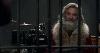 Movie still from “The Christmas Chronicles” (2018), directed by Clay Kaytis – A man with a beard and a fur vest sitting in a cage; Close Up shot, Over the shoulder angle