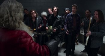 Movie still from “The Christmas Chronicles” (2018), directed by Clay Kaytis – A group of people that are standing up with guitars; Medium shot, Over the shoulder angle
