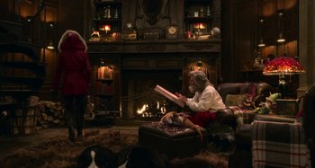 Movie still from “The Christmas Chronicles” (2018), directed by Clay Kaytis – A man sitting in front of a fireplace reading a book; Wide shot, Over the shoulder angle