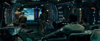 Movie still from “The Cloverfield Paradox” (2018), directed by Julius Onah – A group of people sitting in a room with a large screen; Wide shot, Over the shoulder angle