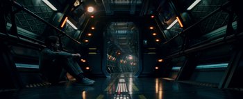 Movie still from “The Cloverfield Paradox” (2018), directed by Julius Onah – A person sitting in a room with lights on the ground; Wide shot, High angle