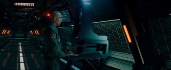 Movie still from “The Cloverfield Paradox” (2018), directed by Julius Onah – A man standing in front of a computer monitor; Medium shot, High angle